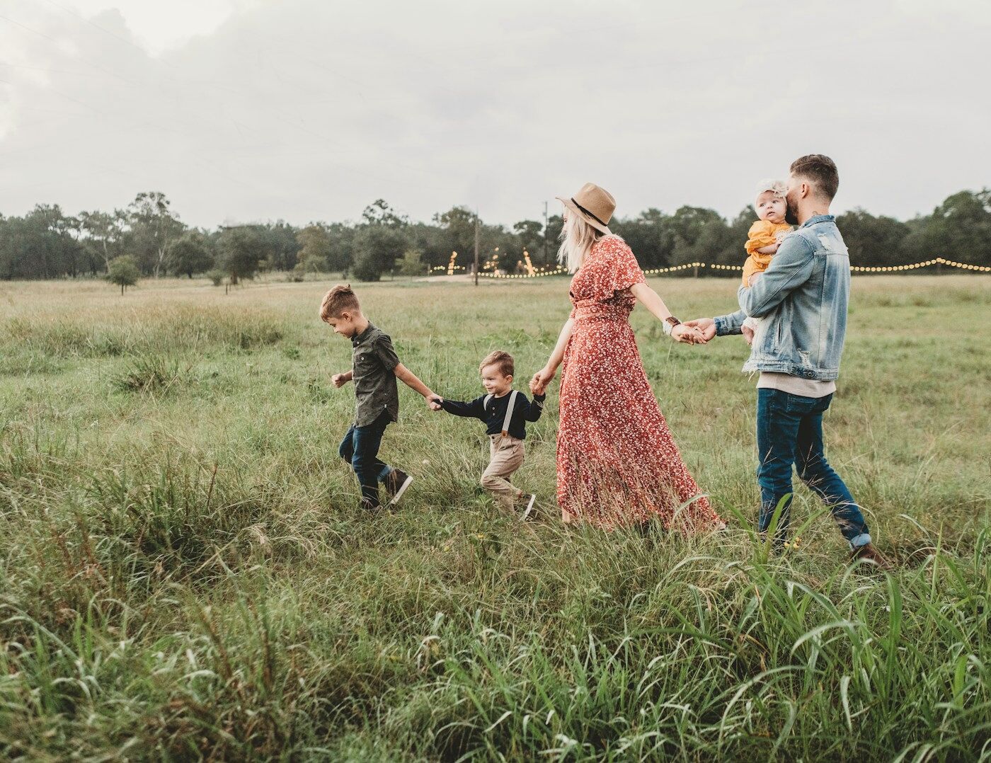A family of five walking hand in hand through a meadow of tall grass in warm evening light, dressed in coordinated autumn tones